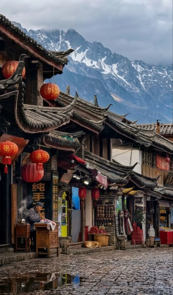 Blick durch eine Gasse in Baisha auf die massiven Berge im Hintergrund