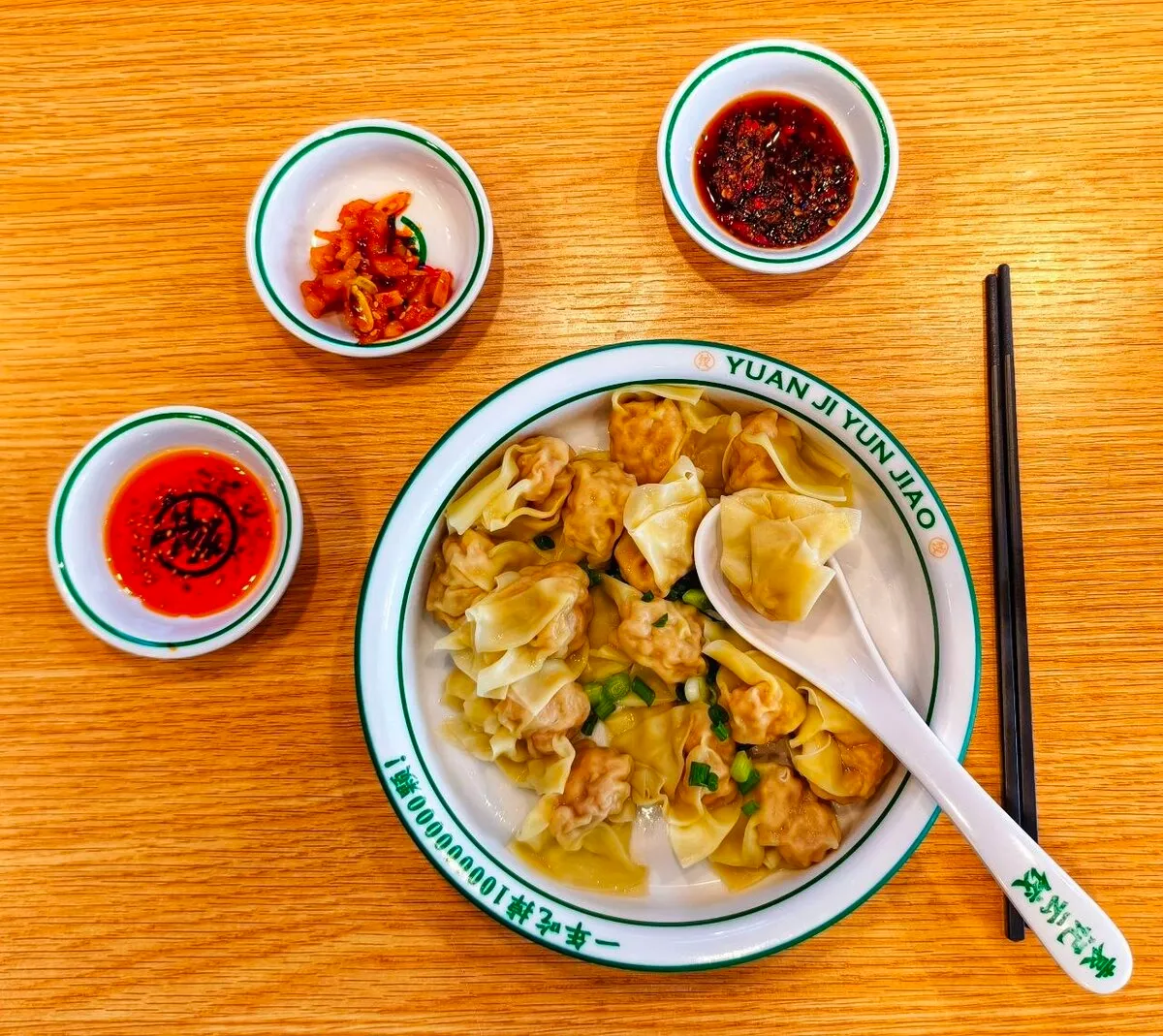 Ein Teller Wontons mit verschiedenen scharfen Saucen auf einem Holztisch
