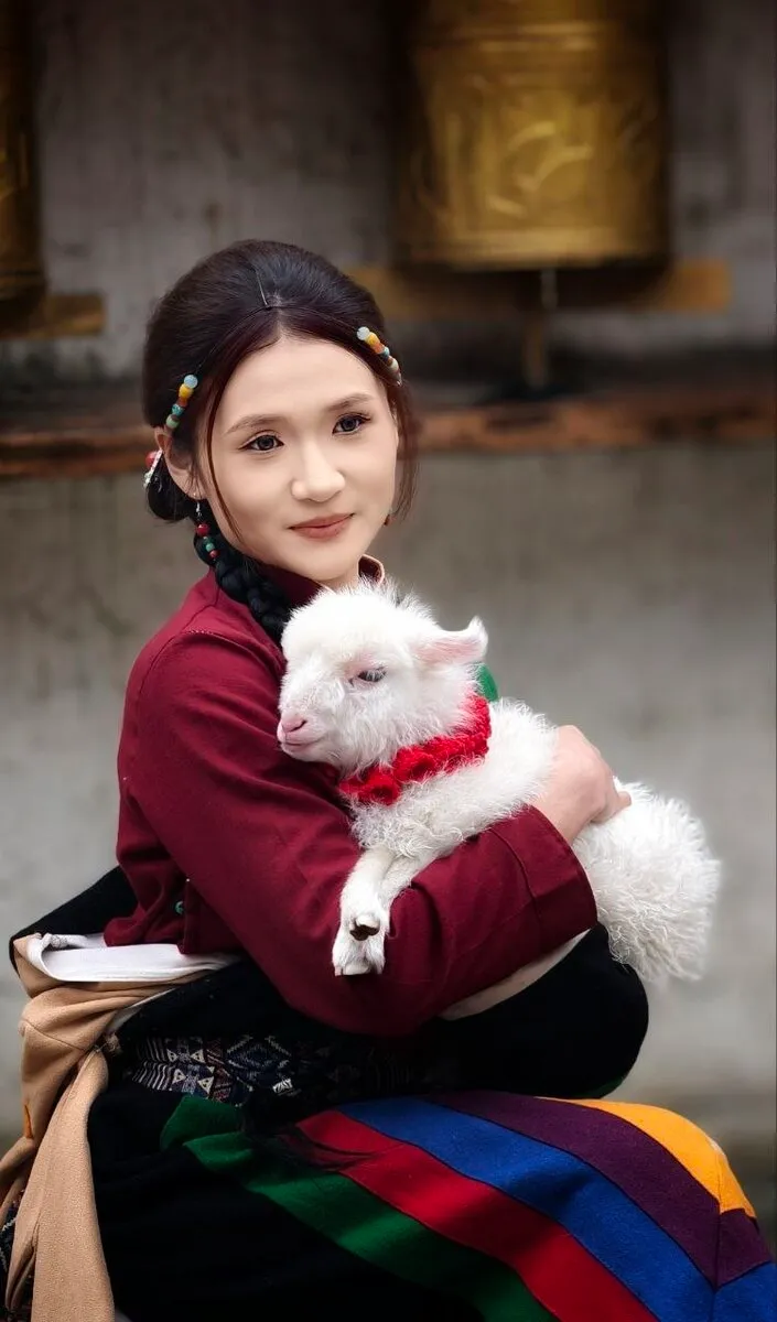 Eine junge Frau in traditioneller Tracht hält ein kleines weißes Lamm im Arm