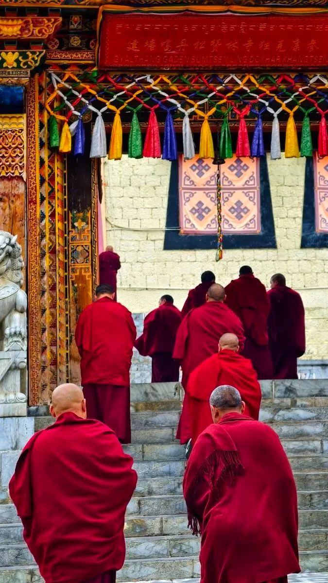 Eine Gruppe von Mönchen in roten Roben steigt eine Treppe zum Tempel hinauf